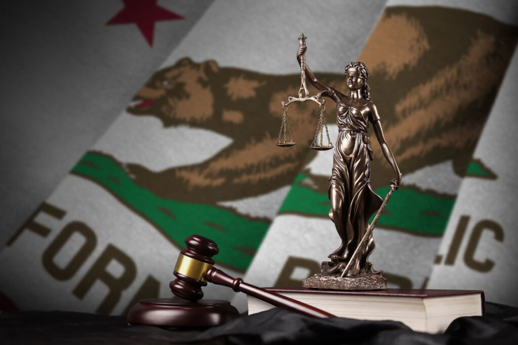 Scales of Justice statuette in front of the state flag of California.