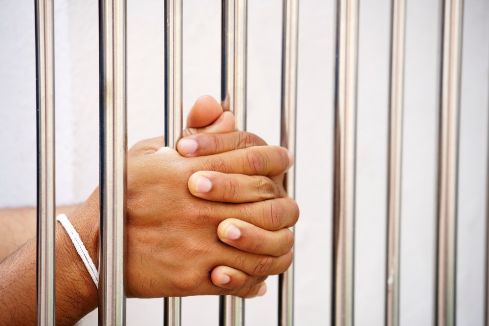 Man behind bars with hands in prayer position