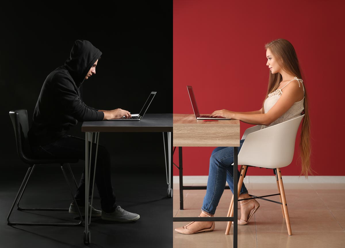 Young woman in white chair using computer talking to a catfishing cyber criminal in dark clothes dark room identity theft