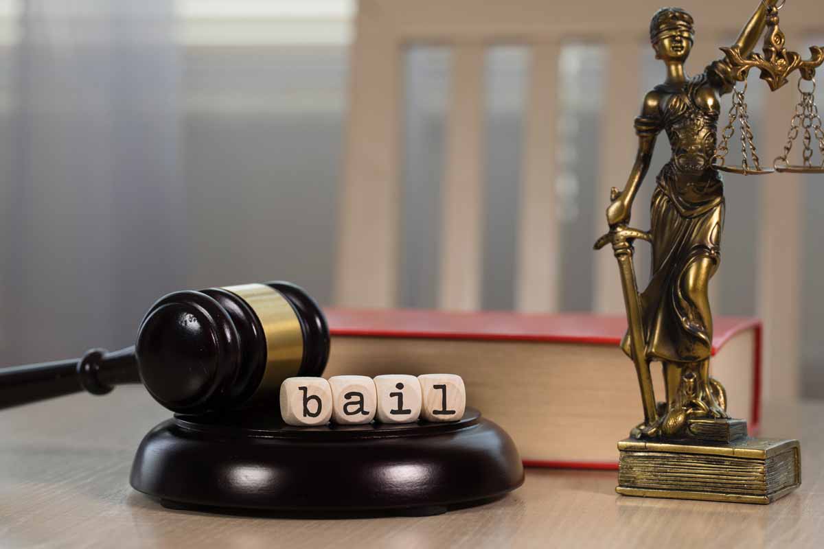 White wooden dices spelling word bail beside justice statue and red law textbook in background