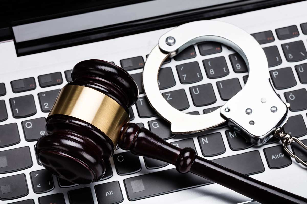 Handcuffs and judges gavel on black keyboard silver laptop cybercrime catfishing