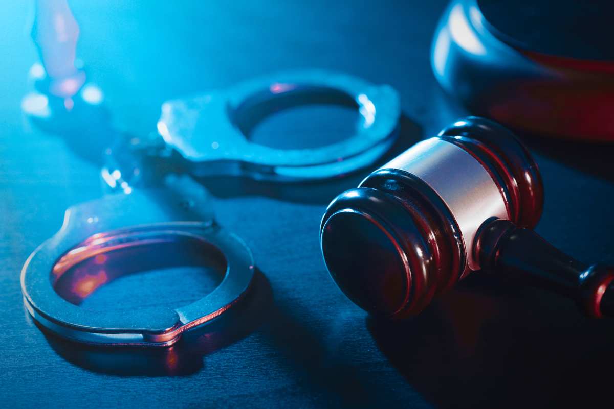 Handcuffs and wooden gavel on table with blue shining light