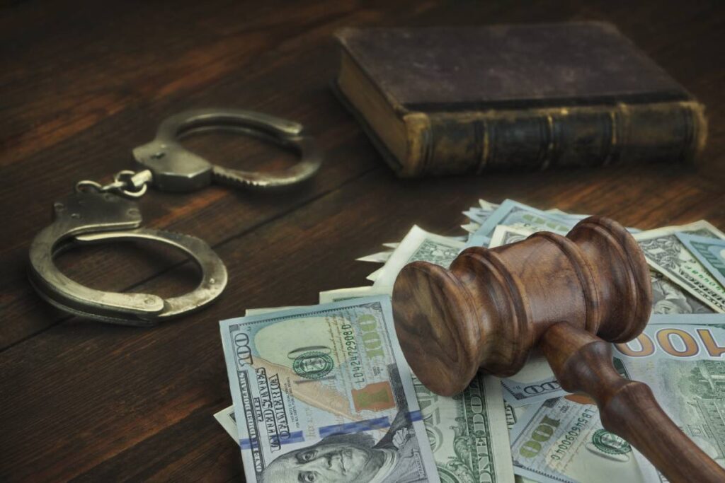Pile of cash on table under wooden gavel with handcuffs in background