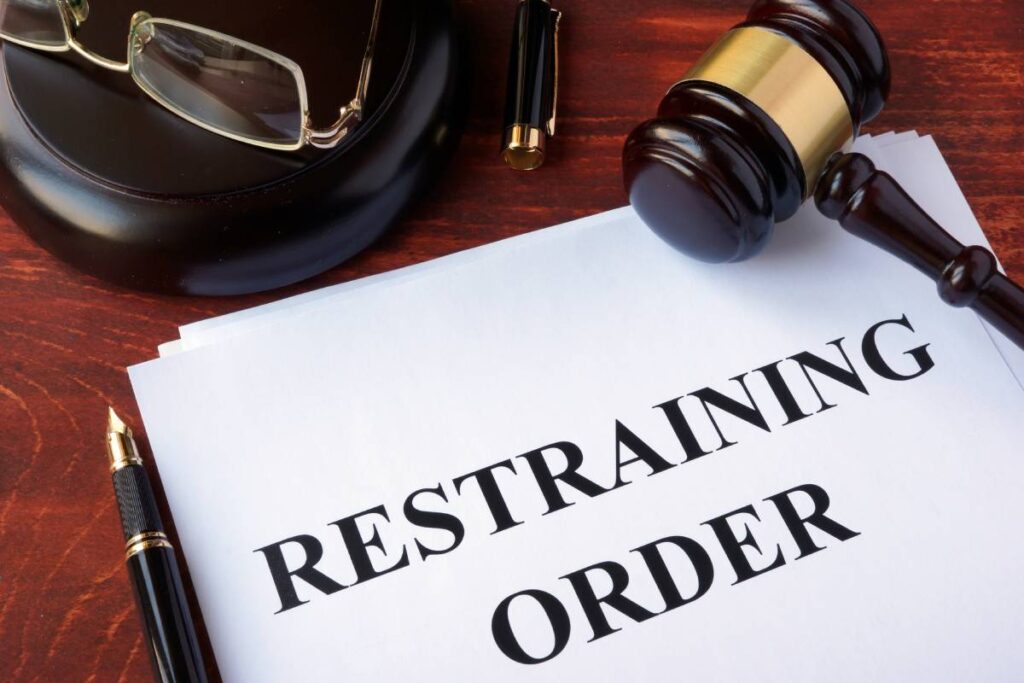 Restraining order in black bold font on white paper with gavel on top and office accessories in background