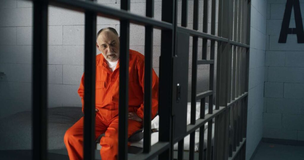 A man in an orange jumpsuit sitting in a jail cell