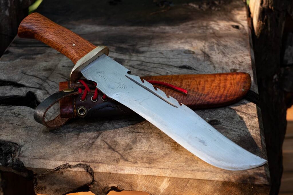 A large Bowie knife lying on a block of wood next to its scabbard.