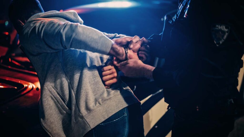 A police officer putting handcuffs on a man behind a car