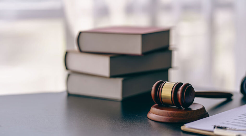 A gavel, base, and law books sit on a table.