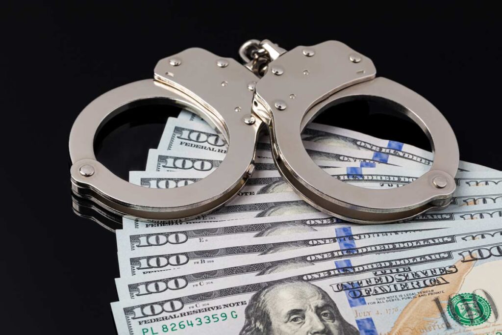 Handcuffs and cash sit on a black table, representing bail bond forfeiture.