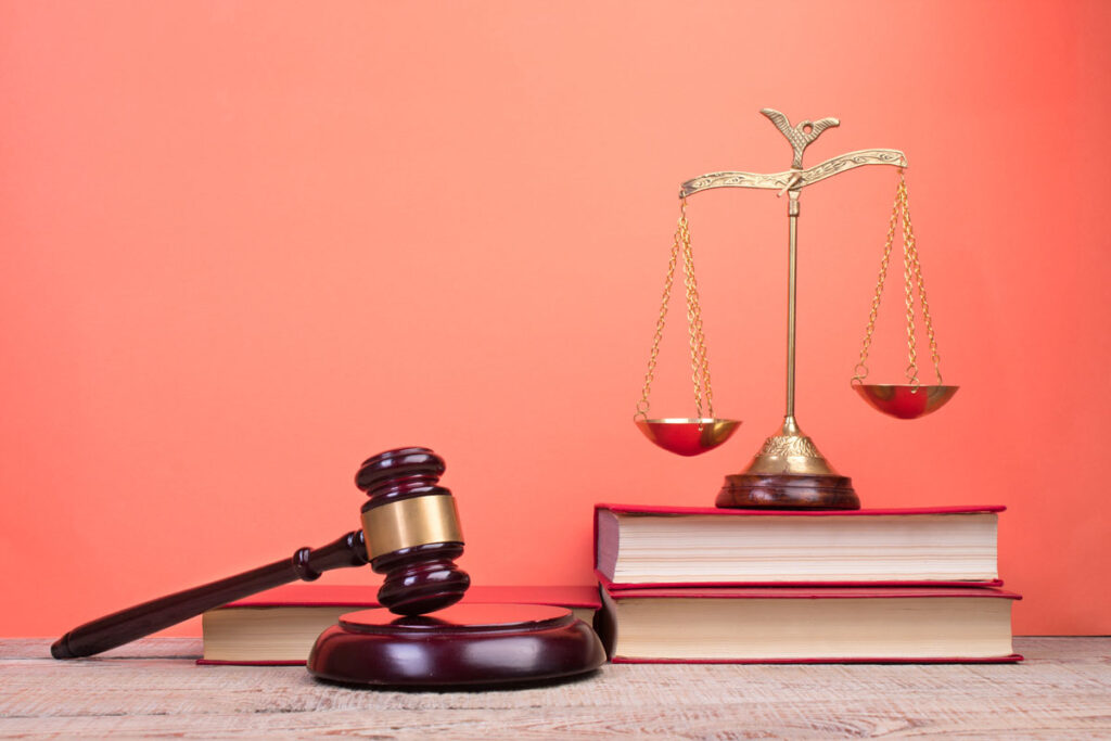 The scales of justice, law books, and a gavel and base sit on a table.