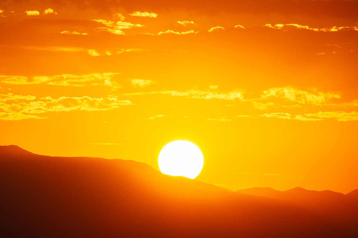 The sun rises from behind mountains in Orange County, CA.