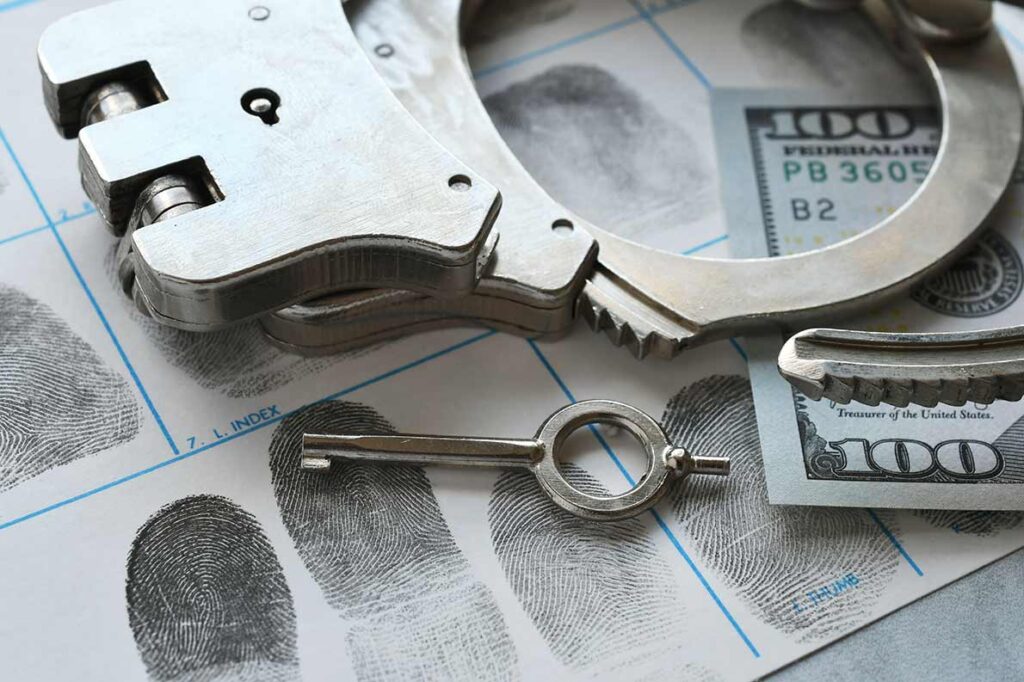 Handcuffs, a key, and a $100 bill on a fingerprint card.