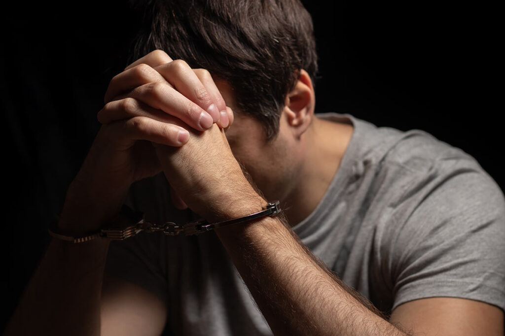 A man, handcuffed hands folded before his lowered head.