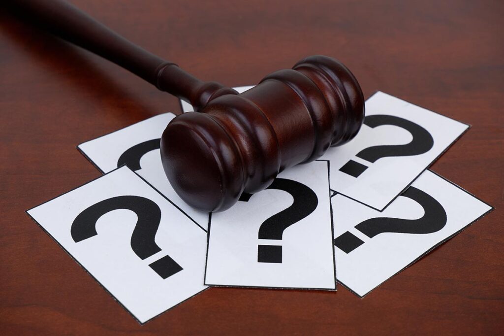 Papers with question marks are scattered below a judge’s gavel.