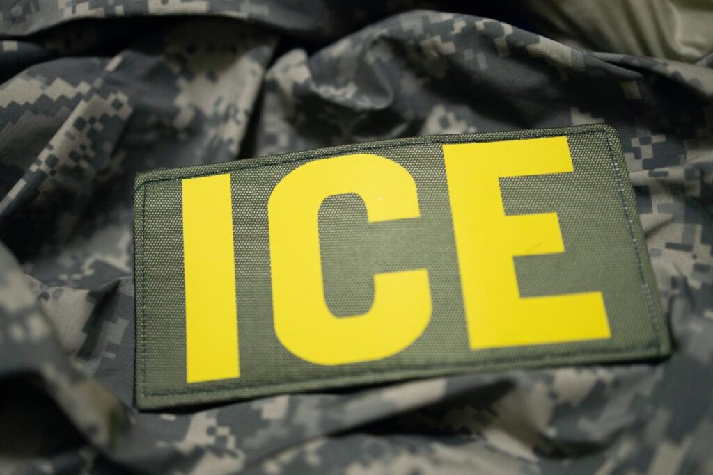 An ICE patch on a camouflage jacket seen close up.