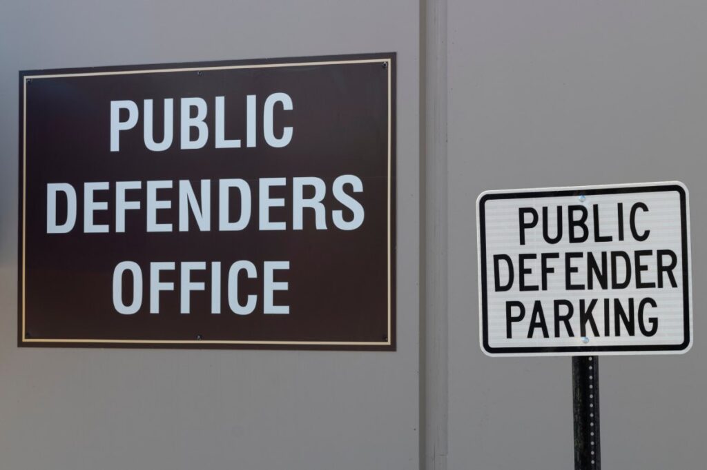 Signs reading “Public Defenders Office” and “Public Defender Parking,” seen on the outside of a building.