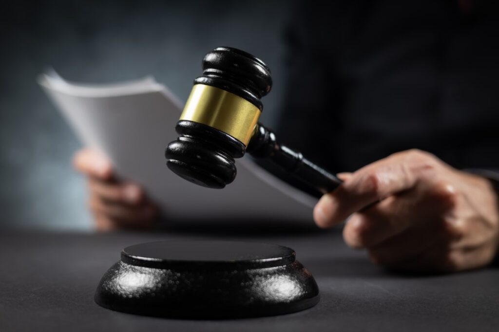 A gavel being hit, while the judge is holding a sheaf of papers.